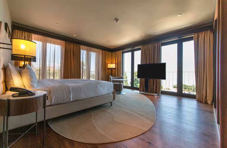 Helles, modernes Hotelzimmer mit einem Bett, Fernseher und großen Fenstern für viel Tageslicht.