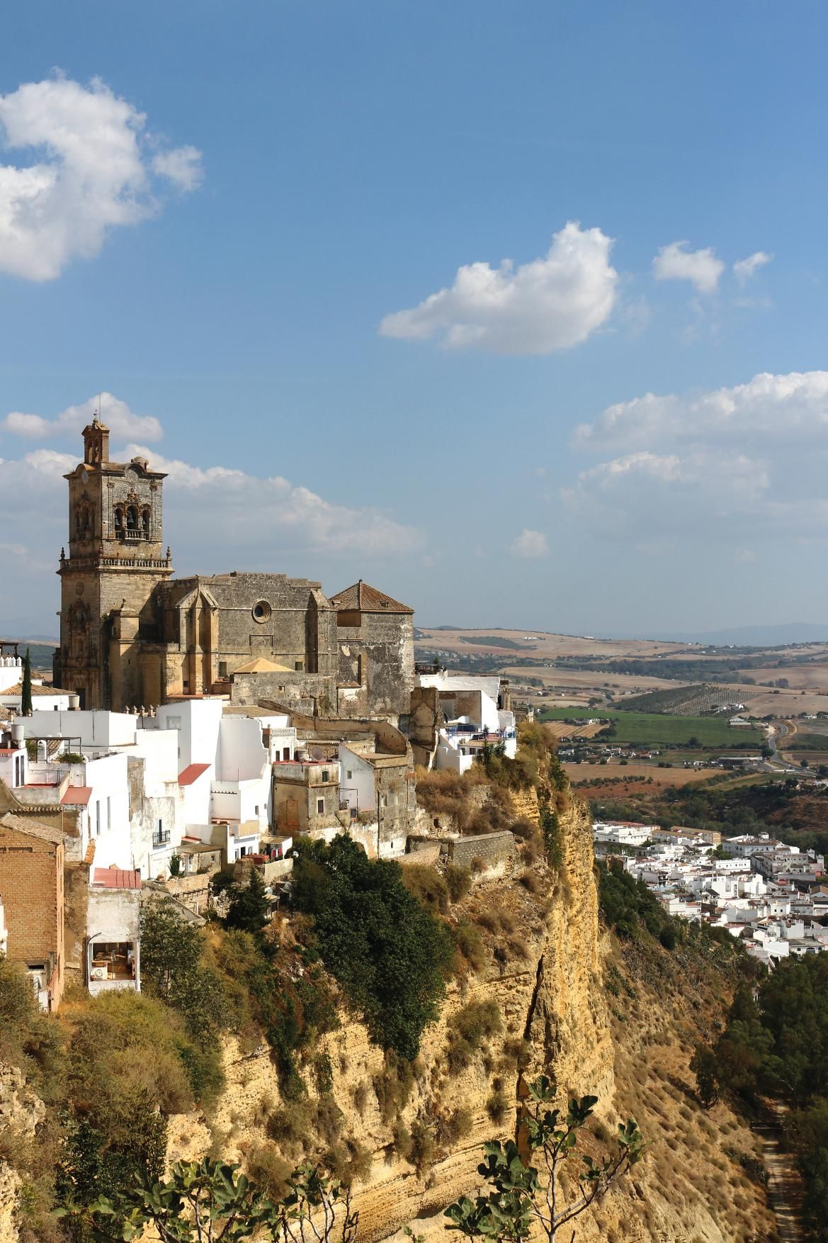 Eine alte Kirche thront auf einer Klippe, umgeben von weißen Häusern und einer malerischen Landschaft.