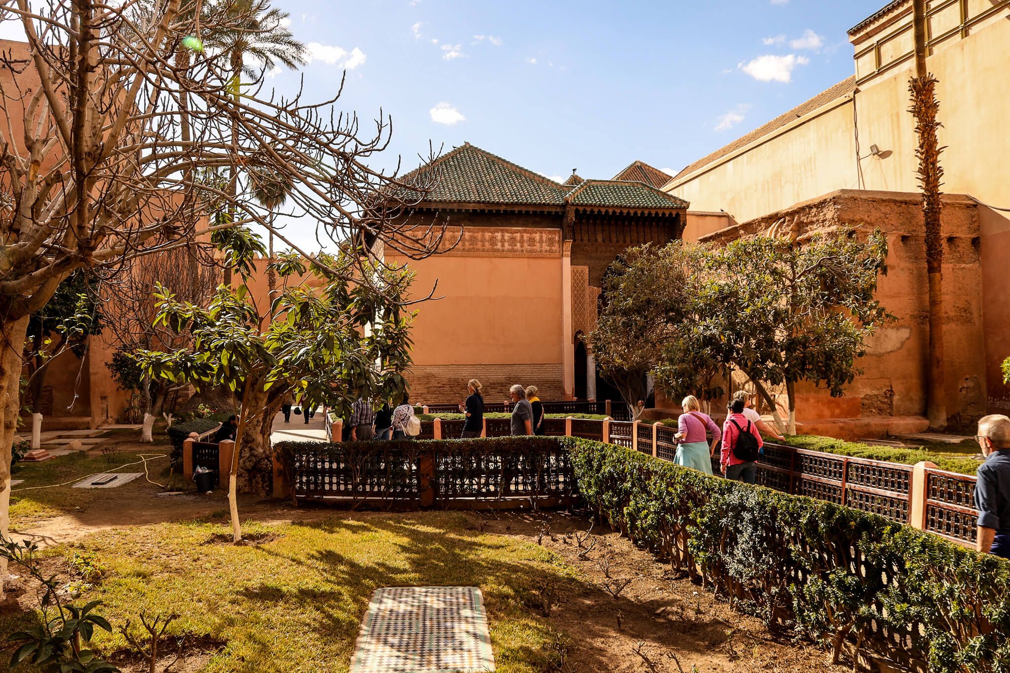 Eine Gruppe von Besuchern erkundet einen ruhigen Garten mit Bäumen und einer schönen Architektur im Hintergrund.